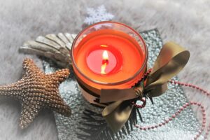 Picture of the Christmas collection "Cinnamon Candle". Picture of a candle with a decorative backdrop including ornaments, bows, snowflakes, and jewlery.